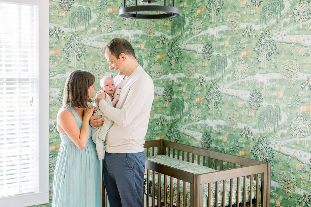 Nicholas's Nursery Photo Session | In-Home Newborn Photography in Tallahassee 1 Parents holding newborn baby boy together in front of green owl and willow nursery wallpaper in Tallahassee